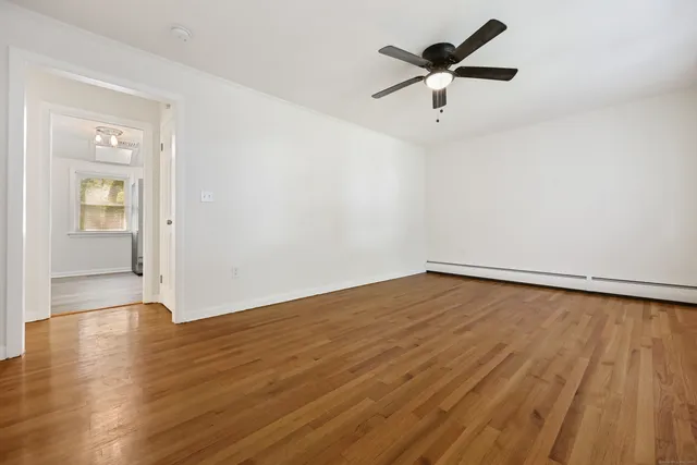 an empty room with wooden floor chandelier fan and windows