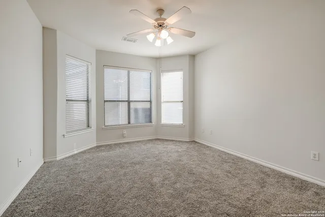 an empty room with chandelier fan and windows