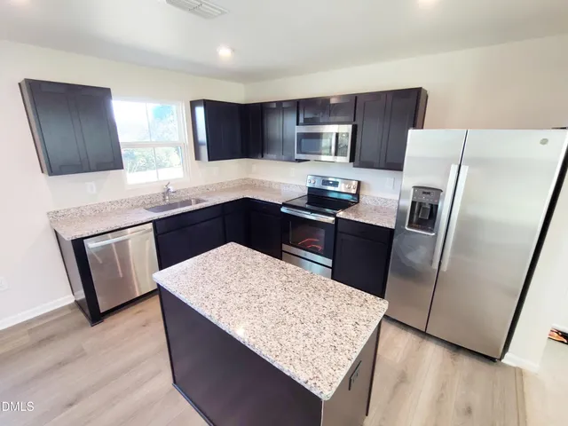 a kitchen with stainless steel appliances kitchen island granite countertop wooden cabinets a refrigerator a sink and dishwasher