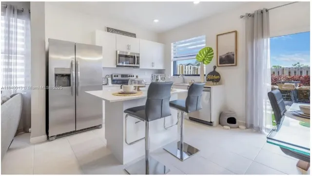 a kitchen with stainless steel appliances kitchen island granite countertop a refrigerator a stove a sink a dining table and chairs with wooden floor