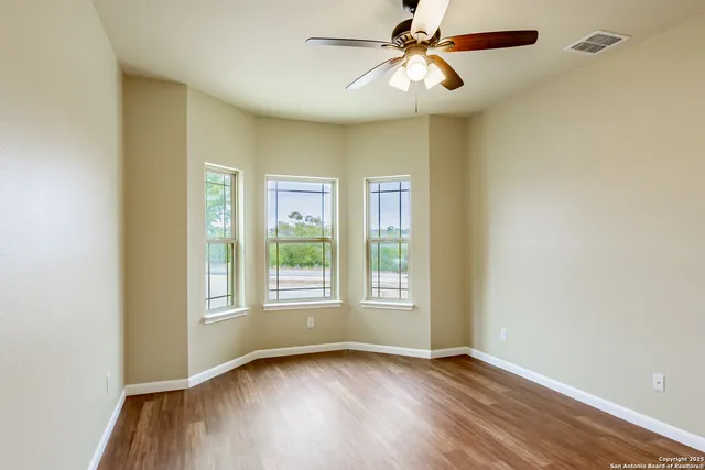 an empty room with wooden floor fan and windows
