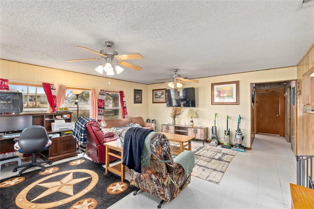 309 Goodwin Street Bangs, TX 76823 - Photo 5 of 20 Living room with wooden walls, tile patterned floors, a ceiling fan, a desk, and a textured ceiling