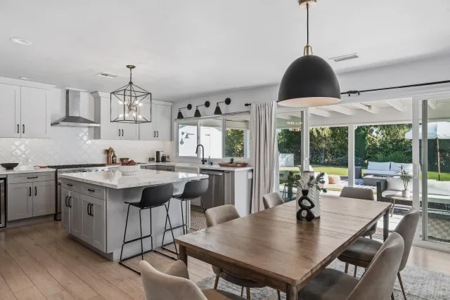 a open kitchen with stainless steel appliances granite countertop a stove a refrigerator a kitchen island a sink dishwasher and white cabinets with wooden floor