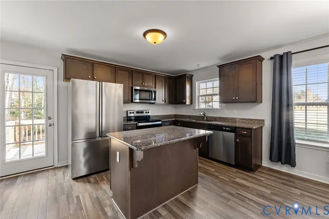 a kitchen with stainless steel appliances granite countertop a refrigerator a stove top oven a sink dishwasher and wooden cabinets with wooden floor
