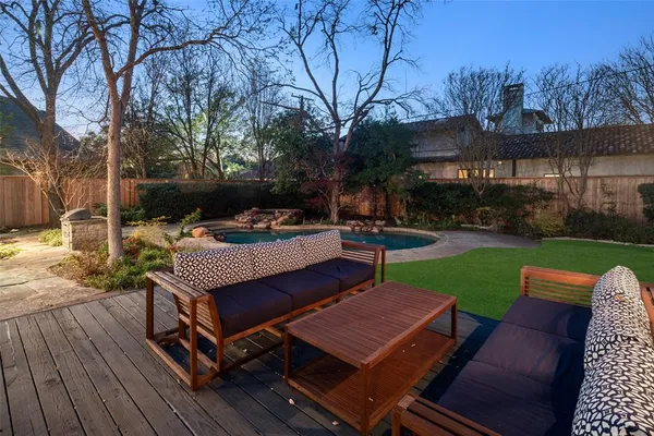 a view of a patio with couches table and chairs under an umbrella with wooden floor and fence