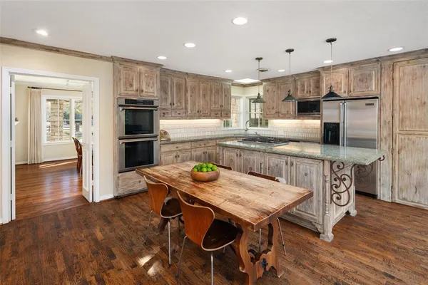 a kitchen with stainless steel appliances granite countertop a table chairs wooden floors and a view of living room