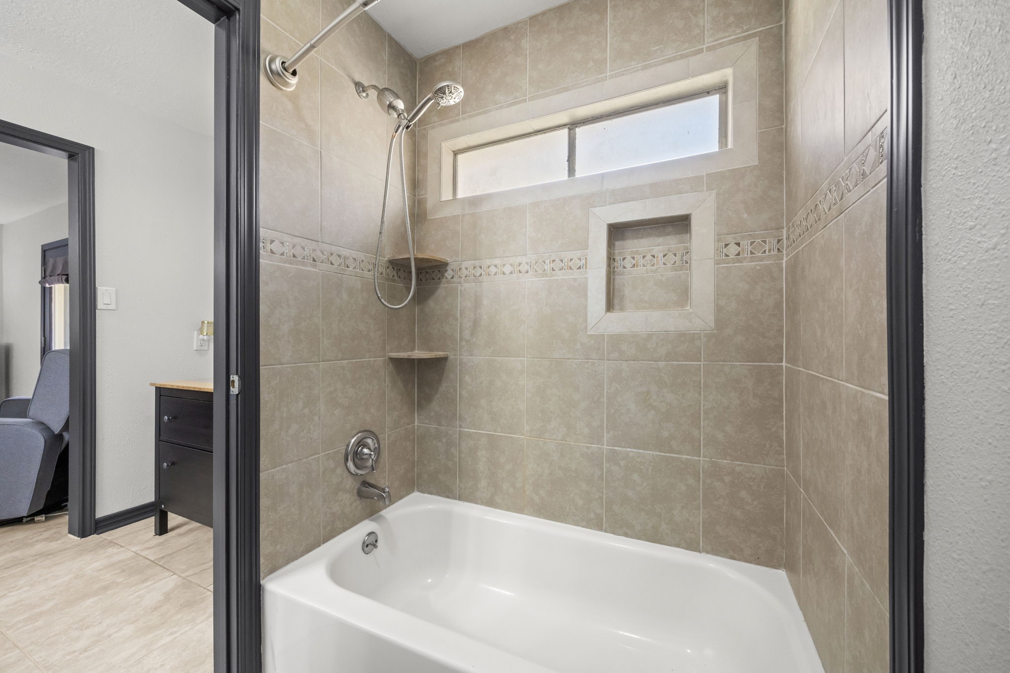 810 Hidden Canyon Road Katy, TX 77450 - Photo 23 of 33 The primary bathroom features a tiled tub/shower combination with neutral tile surround, decorative accent band, and built-in niche for storage. A transom window above the tub allows natural light while maintaining privacy.