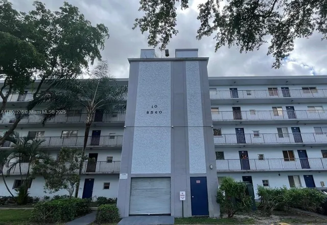 a front view of a building with a garden and trees