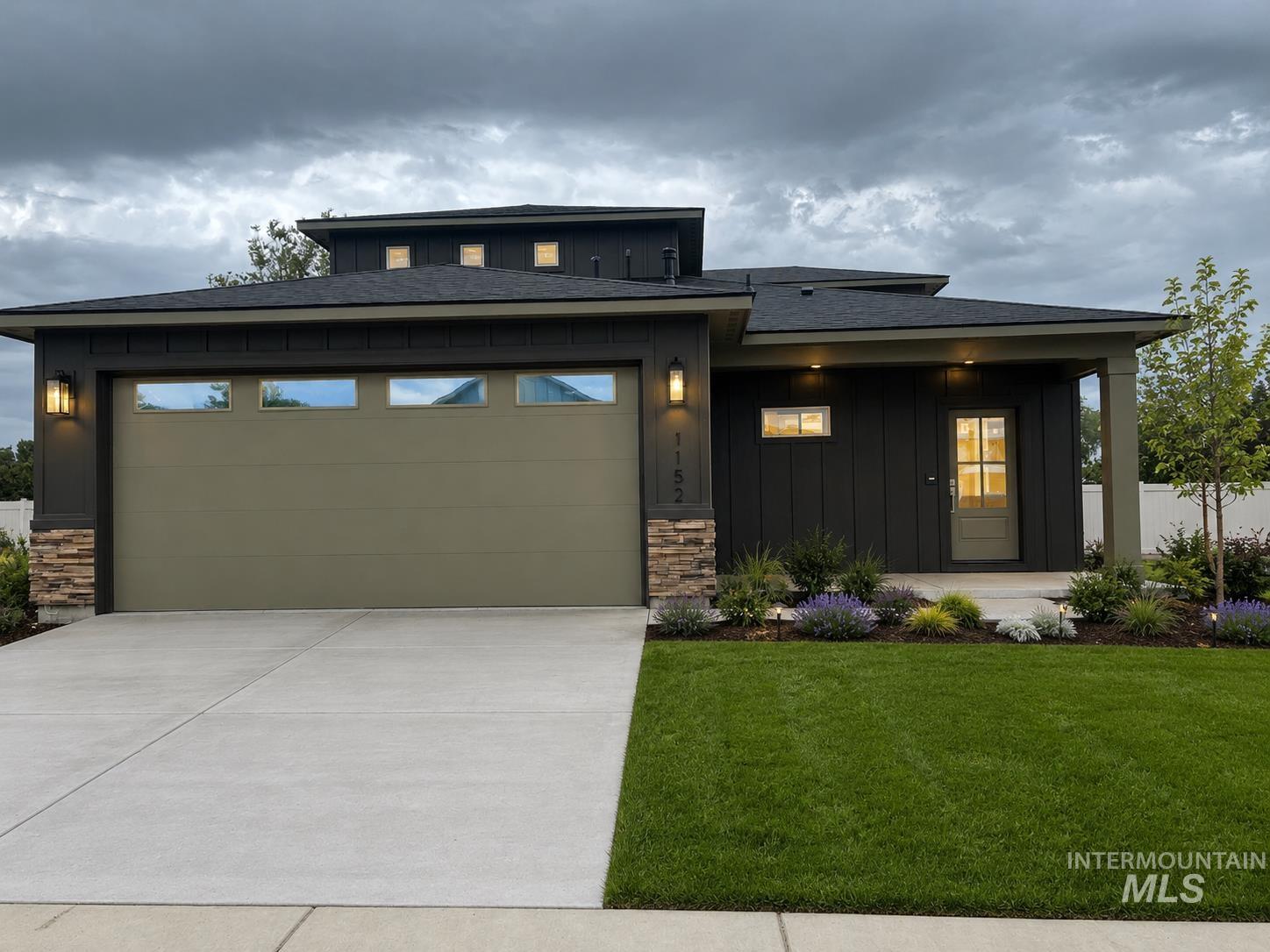 1152 West Recess Way Kuna, ID 83634 - Photo 1 of 3 Contemporary exterior featuring dark horizontal siding, a light olive green garage door with transom windows, and stacked stone accents