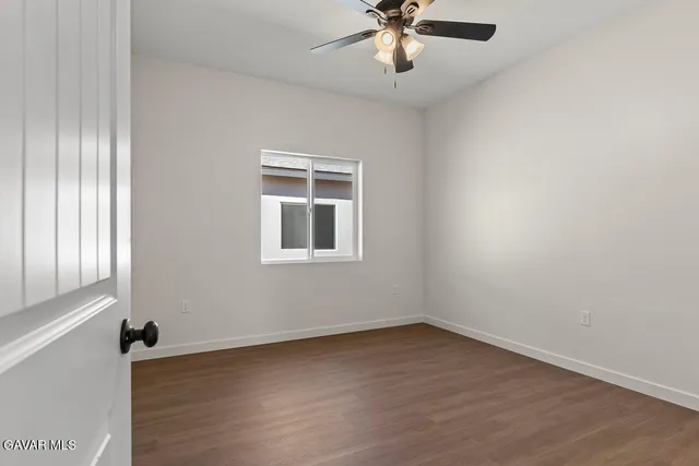 an empty room with wooden floor fan and windows