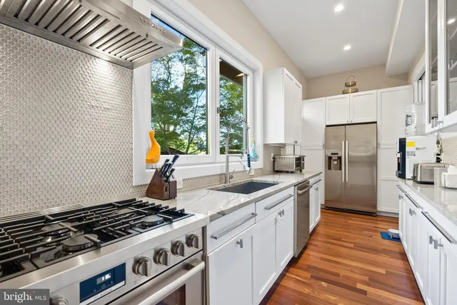 a kitchen with stainless steel appliances granite countertop a stove a sink dishwasher a refrigerator and white cabinets with wooden floor