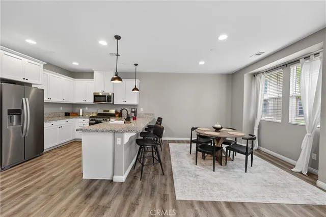 a kitchen with stainless steel appliances kitchen island granite countertop a dining table chairs refrigerator and sink