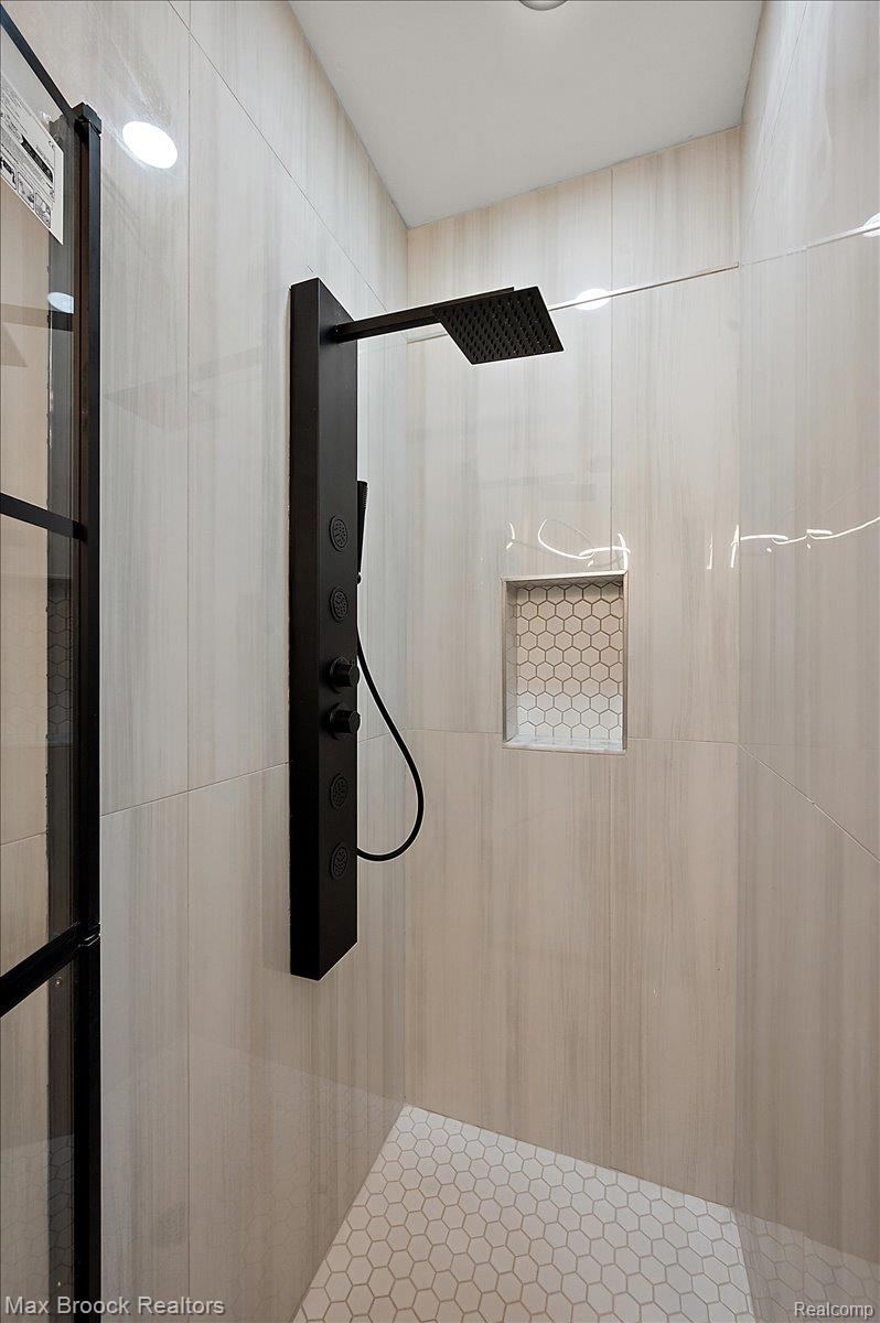4597 Clarkston Road Clarkston, MI 48348 - Photo 42 of 74 Shower enclosure featuring a black shower panel, recessed lighting, light-toned vertical wall tiles, and white hexagonal floor tiles