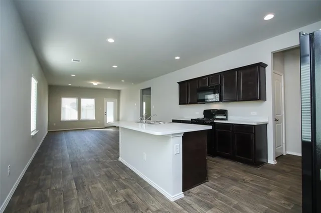 a kitchen with kitchen island stainless steel appliances a sink dishwasher a refrigerator and a stove top oven with wooden floor