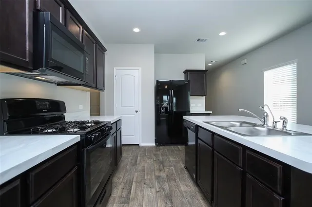 a kitchen with stainless steel appliances kitchen island granite countertop a stove top oven a sink dishwasher a refrigerator and a oven with wooden floor