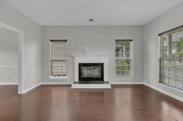 an empty room with wooden floor fireplace and windows