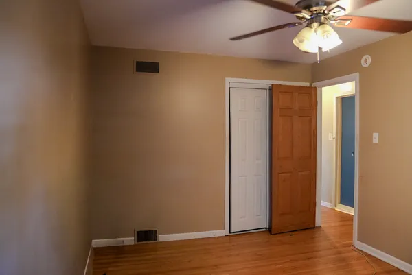 a view of an empty room with wooden floor and a ceiling fan