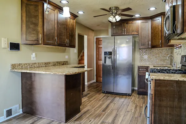 a kitchen with stainless steel appliances granite countertop a refrigerator a oven and a sink with wooden floor
