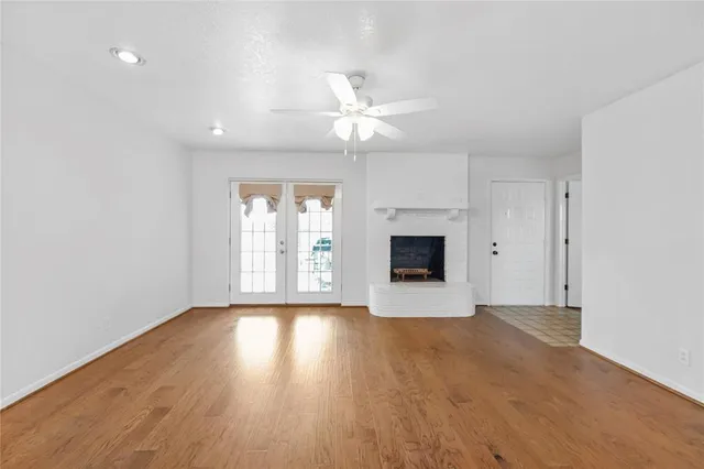 an empty room with wooden floor chandelier fan and windows