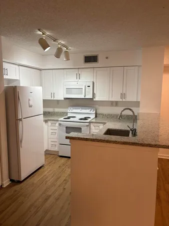 a kitchen with granite countertop a refrigerator sink and white cabinets