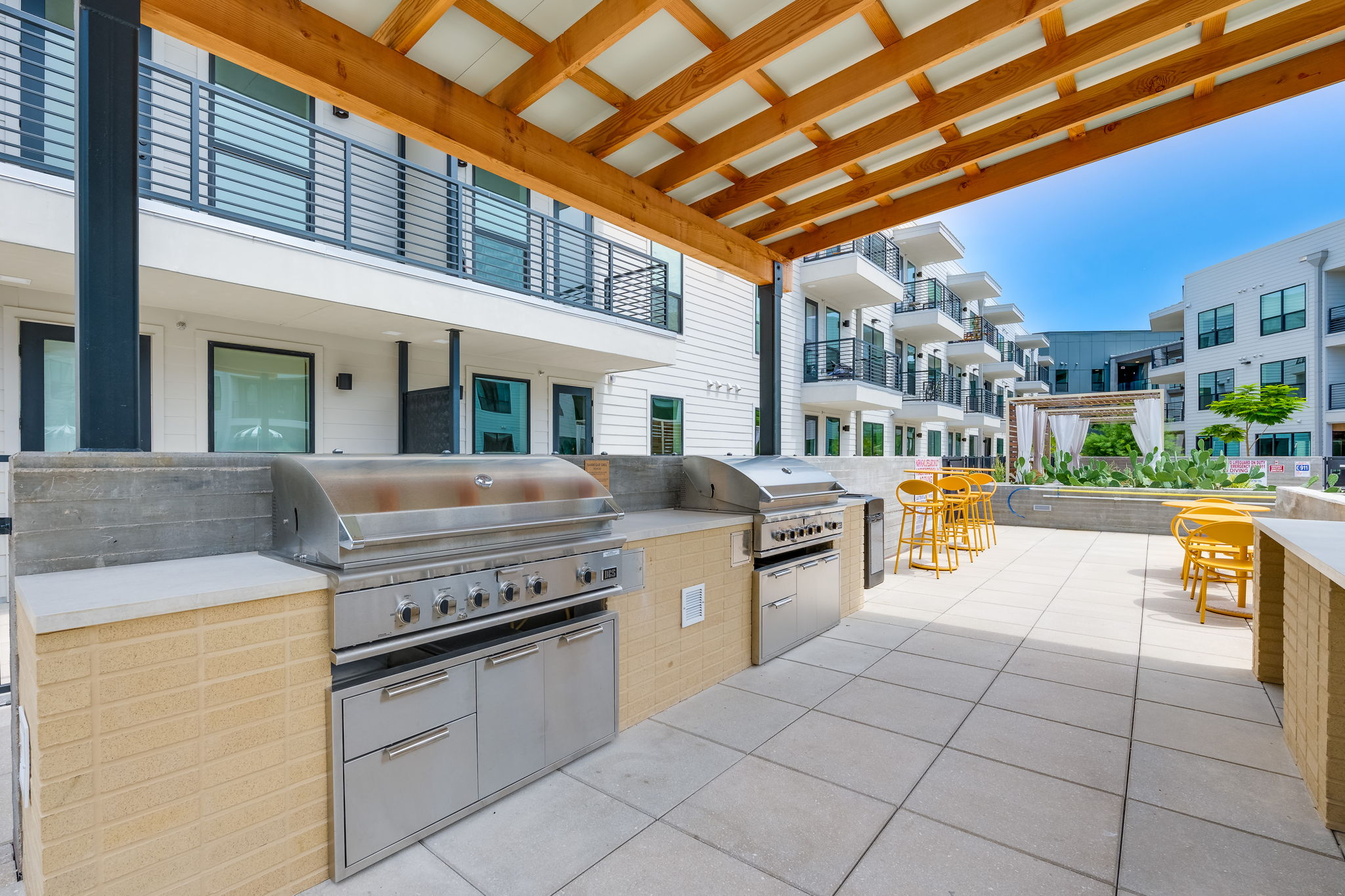 1701 Simond Avenue, Unit 618 Austin, TX 78723 - Photo 21 of 38 Outdoor kitchen area with two stainless steel grills, a light-toned wood pergola, and a tiled patio