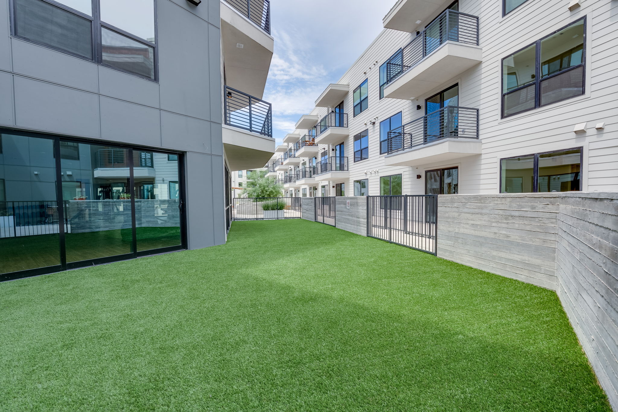 1701 Simond Avenue, Unit 618 Austin, TX 78723 - Photo 32 of 38 Expansive green space featuring artificial turf, bordered by a concrete retaining wall and a black metal fence