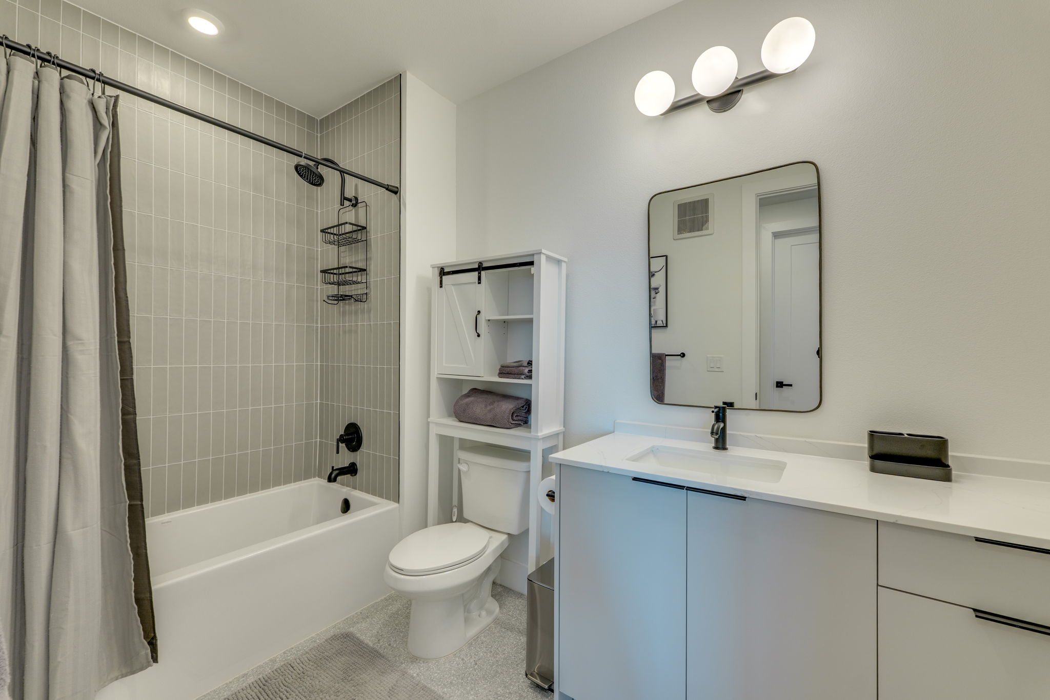1701 Simond Avenue, Unit 618 Austin, TX 78723 - Photo 8 of 38 The bathroom features a white vanity with a white countertop and a rectangular undermount sink, a large mirror with a black frame, and a bathtub with light gray subway tile walls