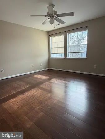 an empty room with wooden floor ceiling fan and windows