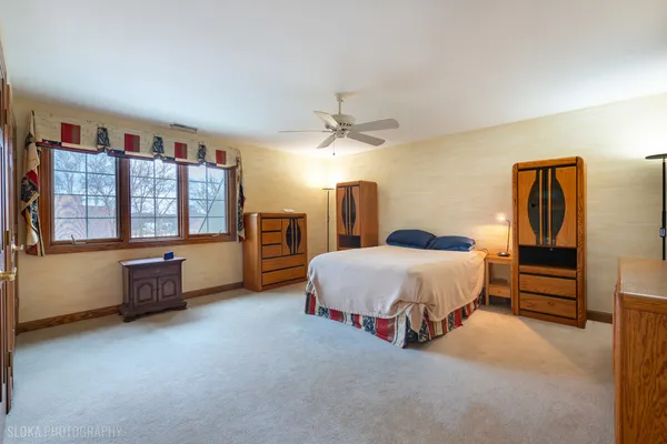 a spacious bedroom with a bed a dresser and large windows