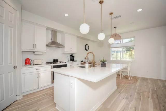 a kitchen with stainless steel appliances kitchen island a white stove top oven a sink dishwasher and white cabinets with wooden floor