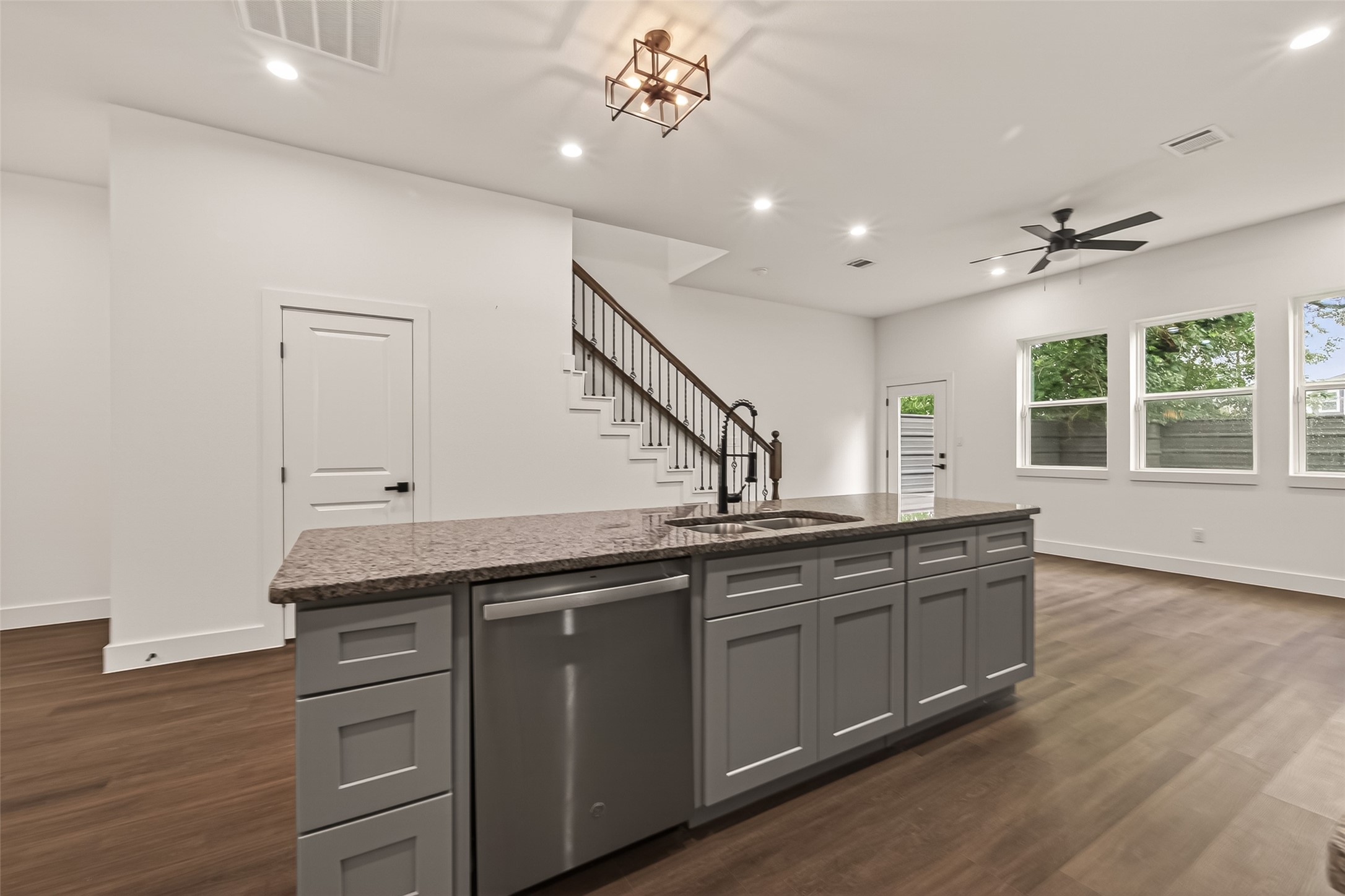 6808 Madrid Street Houston, TX 77021 - Photo 12 of 31 This spacious, open-concept living area features modern finishes with a large kitchen island, sleek cabinetry, and stainless steel appliances. The room is well-lit by natural light through multiple windows, and includes a stylish staircase and dark wood flooring.