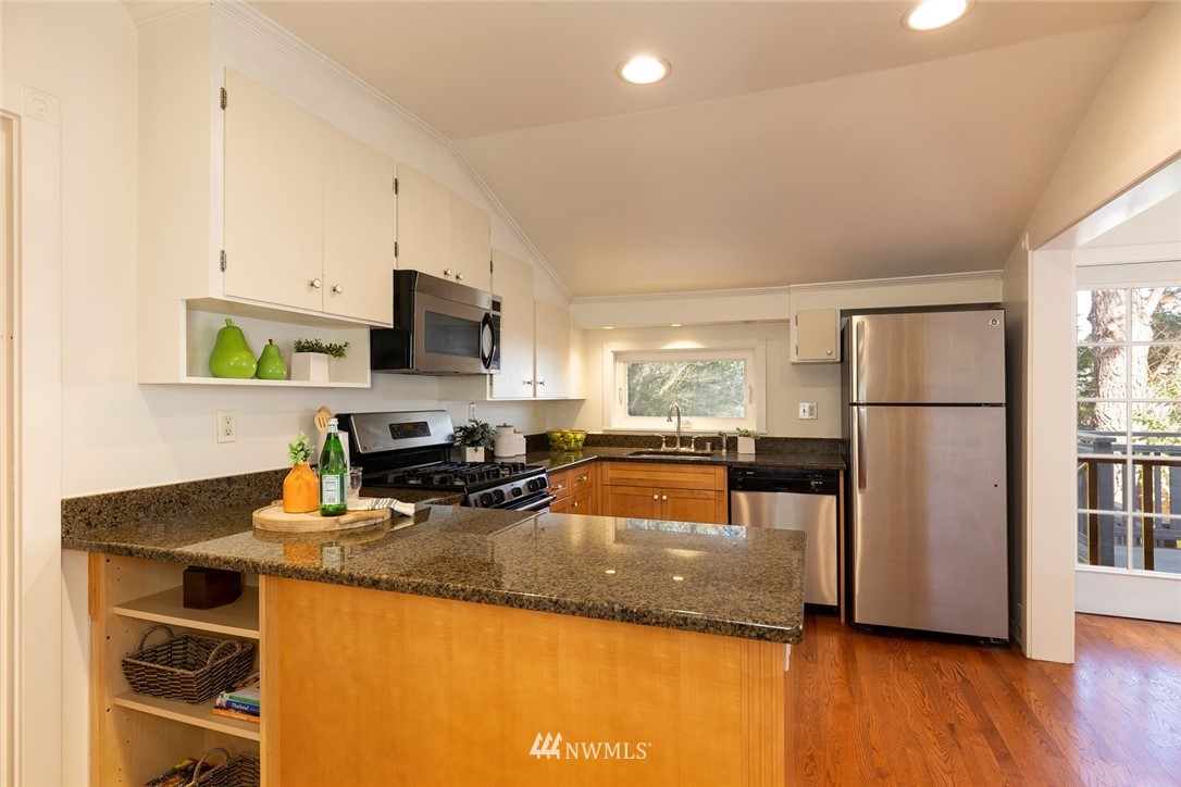 708 North 63rd Street Seattle, WA 98103 - Photo 9 of 24 a kitchen with granite countertop a refrigerator a stove and a sink with wooden floor