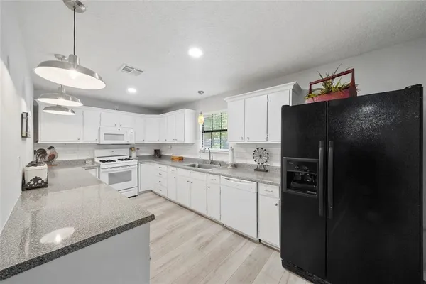 a kitchen with stainless steel appliances granite countertop a refrigerator a sink dishwasher a stove and white cabinets with wooden floor