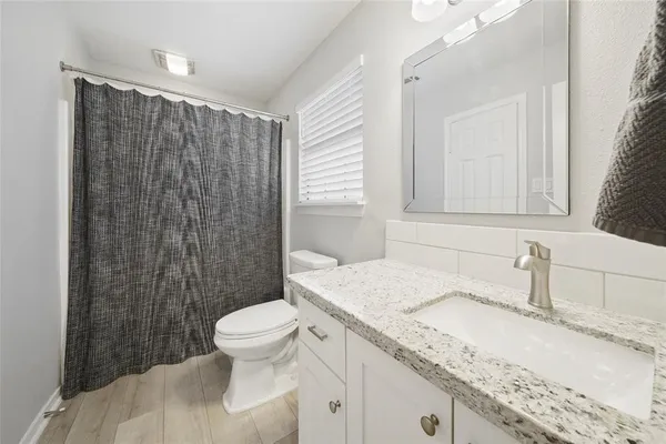 a bathroom with a granite countertop sink a toilet a mirror and shower curtain