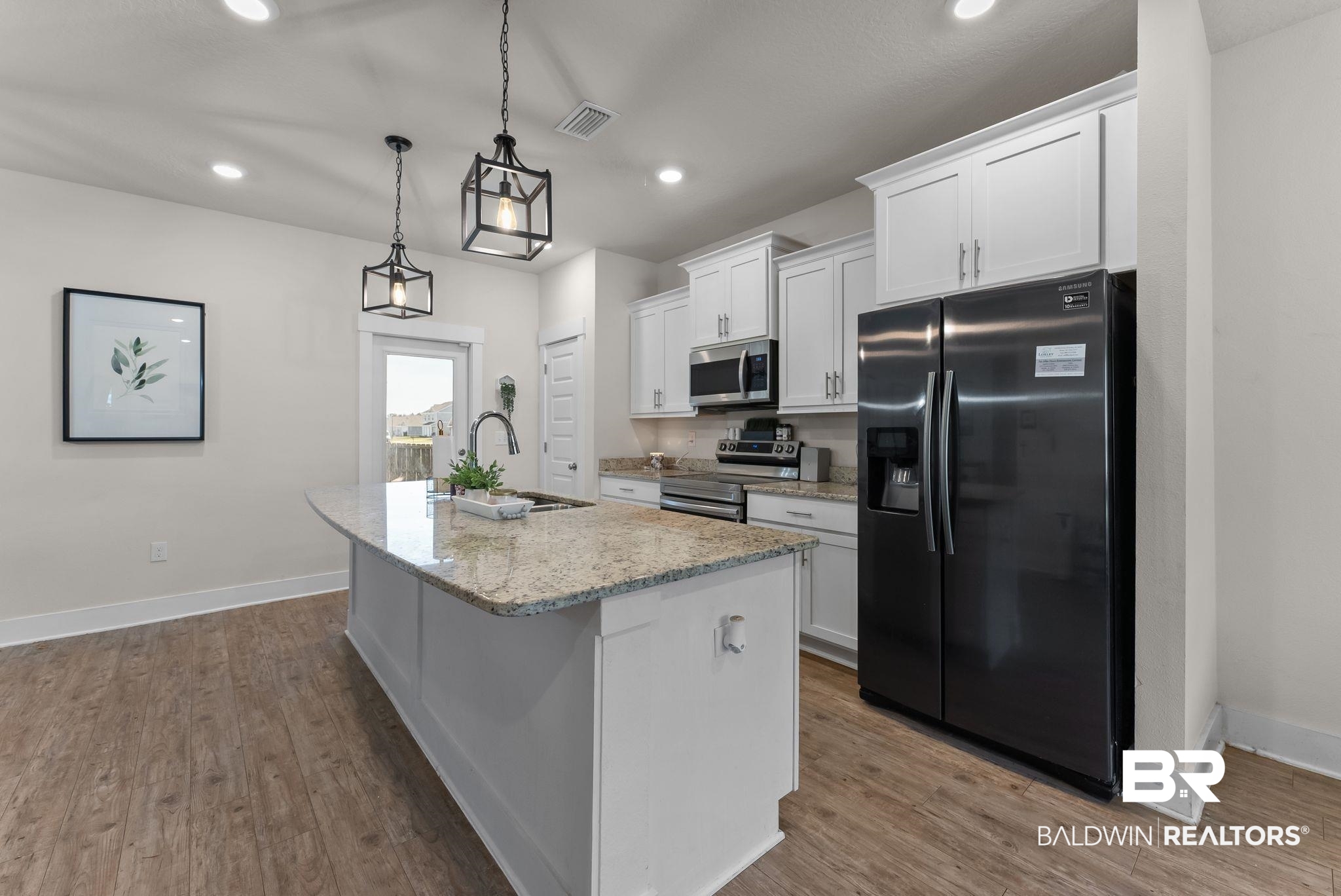 16607 Prado Loop Loxley, AL 36551 - Photo 12 of 46 Kitchen featuring a curved central island with a stone countertop and undermount sink, pendant lighting, wood-finish flooring, white cabinetry, and stainless steel appliances