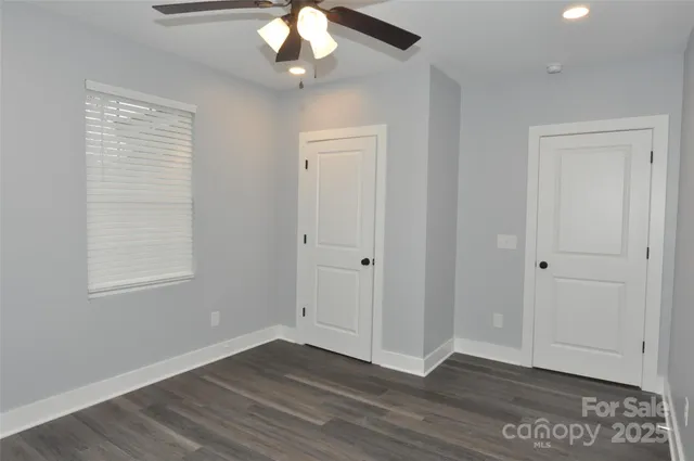 an empty room with wooden floor chandelier fan and windows