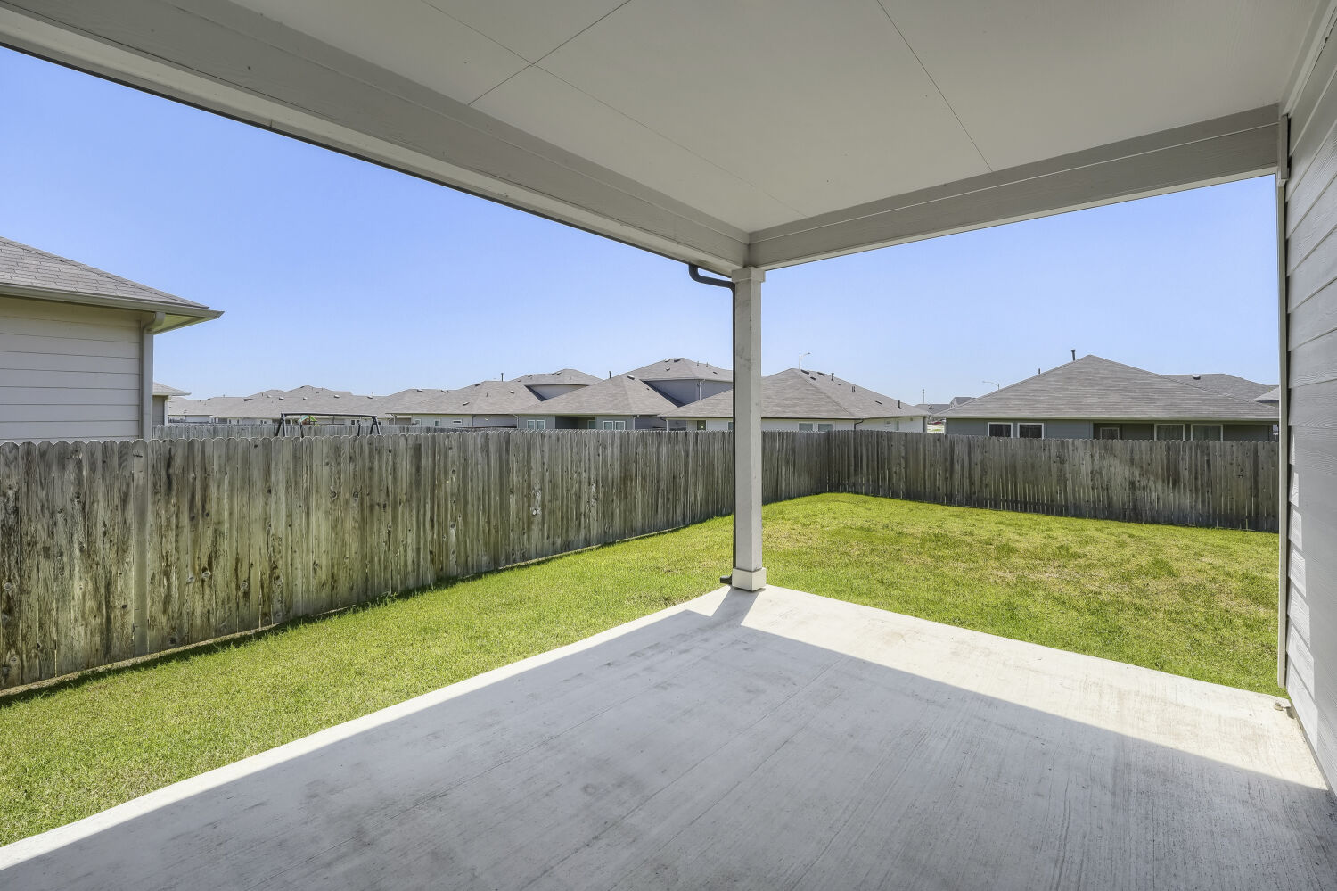 13507 Howser Trace Manor, TX 78653 - Photo 23 of 28 A spacious backyard with a private wooden fence, a manicured lawn, and a covered concrete patio.