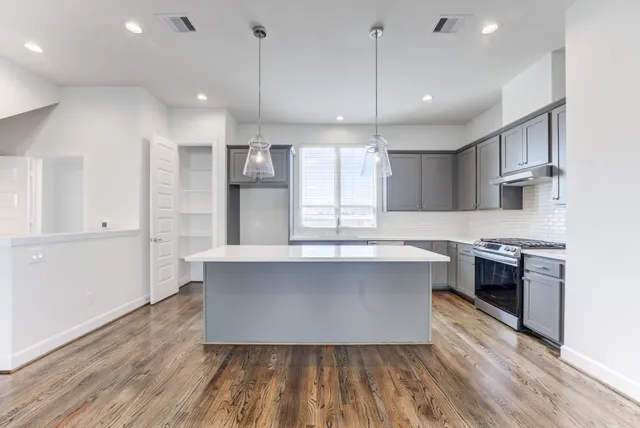 a large kitchen with stainless steel appliances a large counter top a stove and a wooden floors