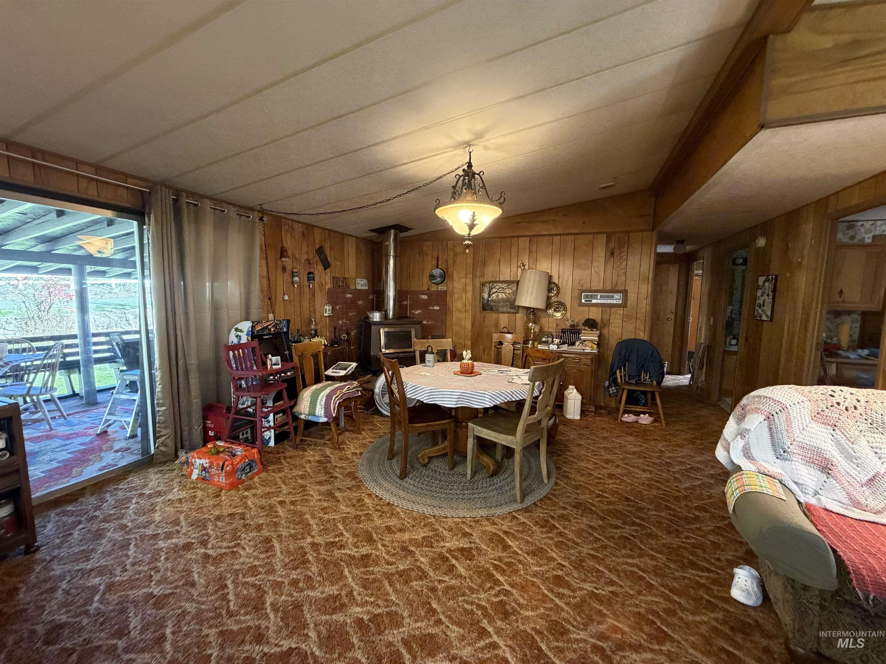 27474 North Tom Beall Road Lapwai, ID 83540 - Photo 29 of 50 Dining room with a wood stove, vaulted ceiling, dark colored carpet, and wooden walls