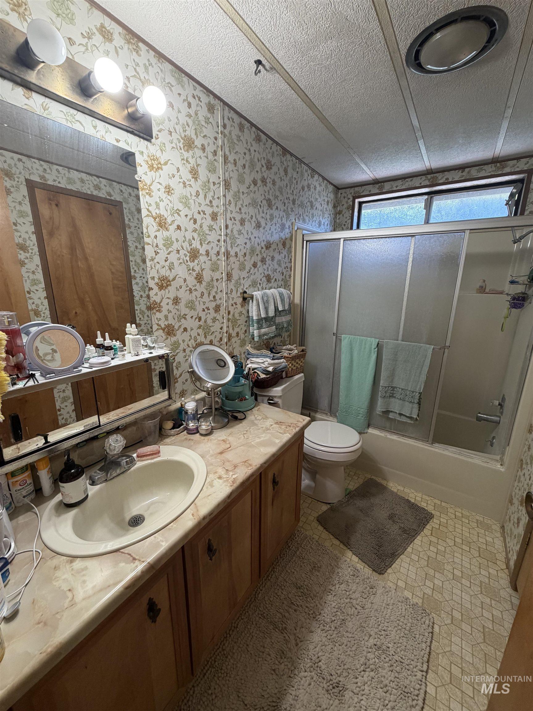 27474 North Tom Beall Road Lapwai, ID 83540 - Photo 34 of 50 Bathroom with vanity, combined bath / shower with glass door, a textured ceiling, and wallpapered walls