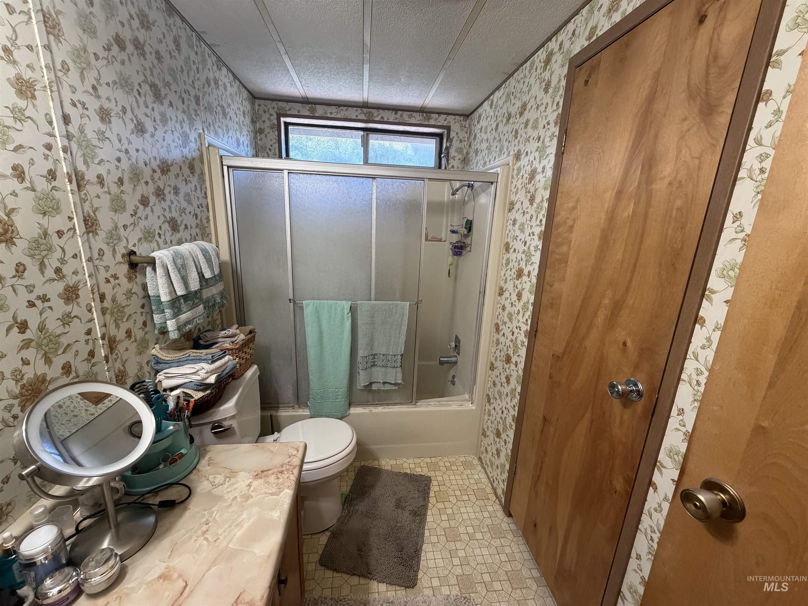 27474 North Tom Beall Road Lapwai, ID 83540 - Photo 35 of 50 Bathroom featuring enclosed tub / shower combo, a textured ceiling, vanity, light tile patterned floors, and wallpapered walls