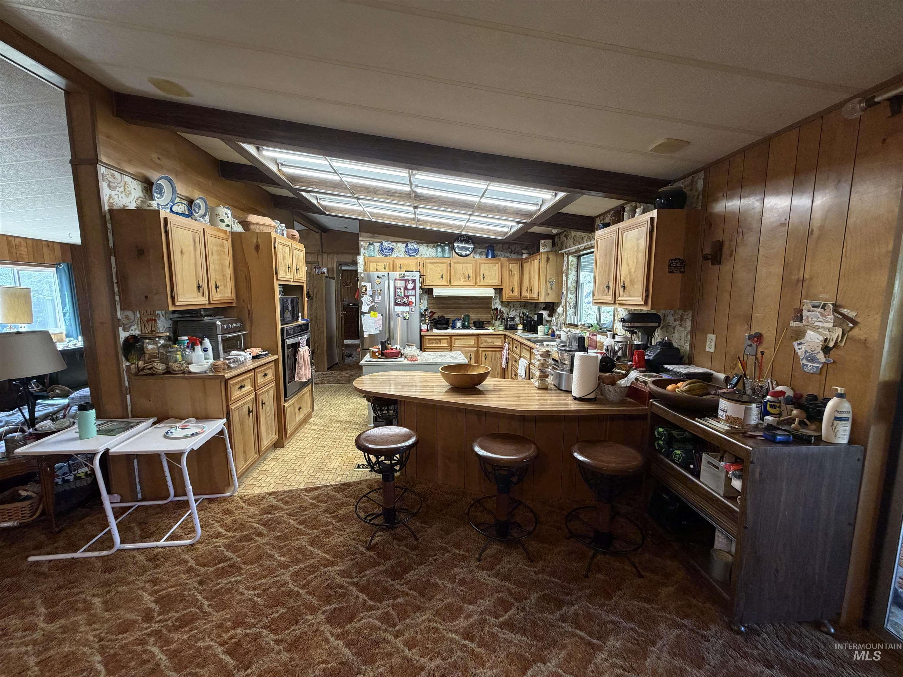 27474 North Tom Beall Road Lapwai, ID 83540 - Photo 39 of 50 Kitchen featuring wood walls, a peninsula, dark colored carpet, stainless steel appliances, and a breakfast bar