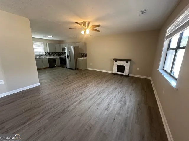 an empty room with wooden floor kitchen view and a window