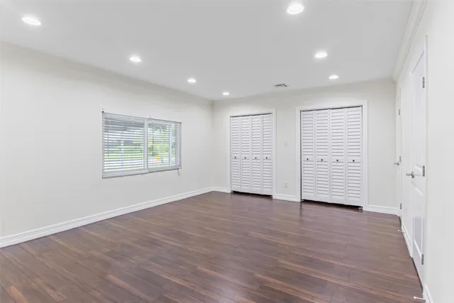 an empty room with wooden floor closet and windows
