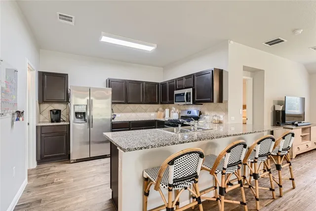 a kitchen with stainless steel appliances granite countertop a sink a stove a refrigerator cabinets and chairs