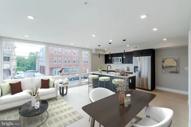 a living room with stainless steel appliances furniture a rug and a kitchen view