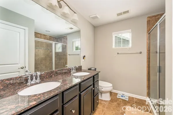 a bathroom with a granite countertop double vanity sink a mirror and a toilet