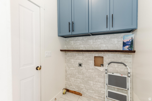972 West 2840th Street South Logan, UT 84321 - Photo 11 of 46 Laundry area featuring blue upper cabinetry with matte black hardware, white brick-patterned wall, and a dark wood floating shelf