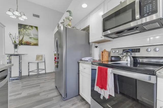 a kitchen with stainless steel appliances granite countertop a refrigerator a stove and a sink with wooden floor