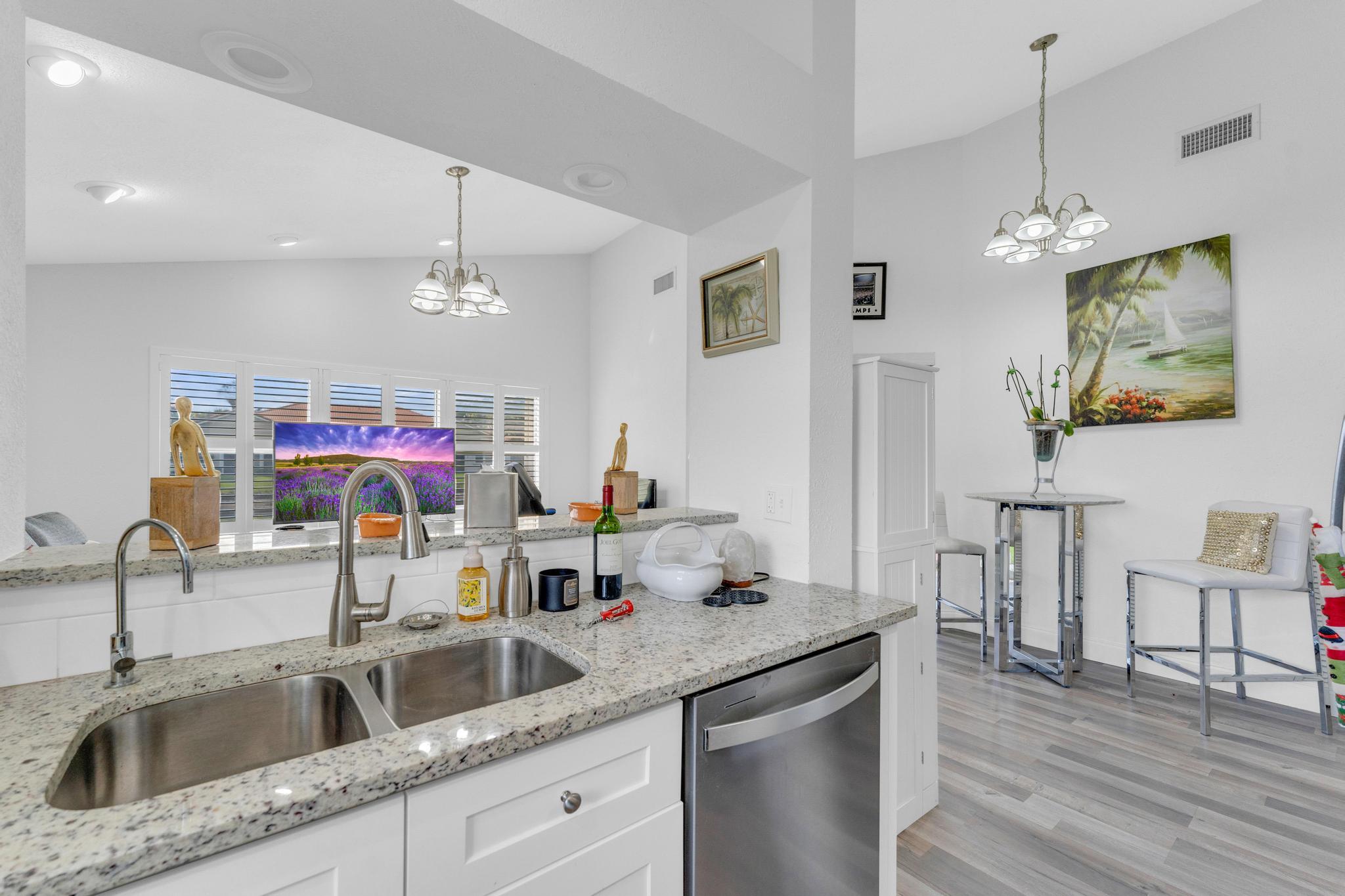 11120 Sangria Court Boca Raton, FL 33498 - Photo 9 of 34 a kitchen with a sink dishwasher a dining table and chairs with wooden floor